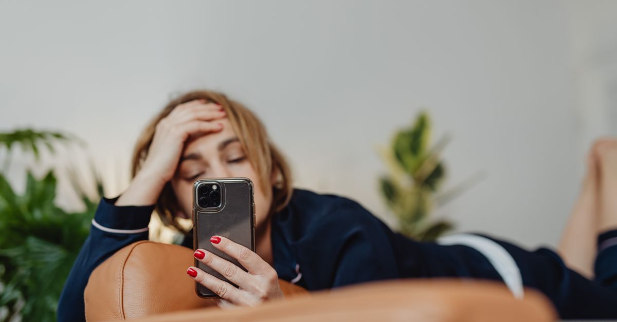 Frau auf dem Sofa mit Smartphone vor dem Gesicht, zum Thema Foto-Tresor für private Bilder.