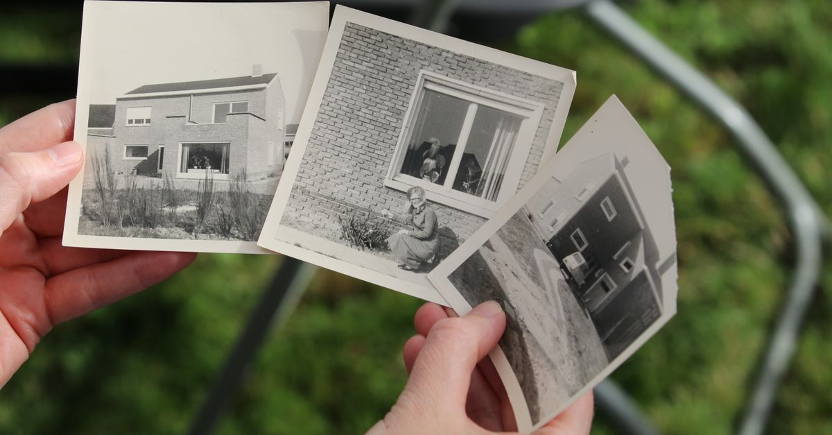 Hands holding vintage black and white photos of old houses outdoors.