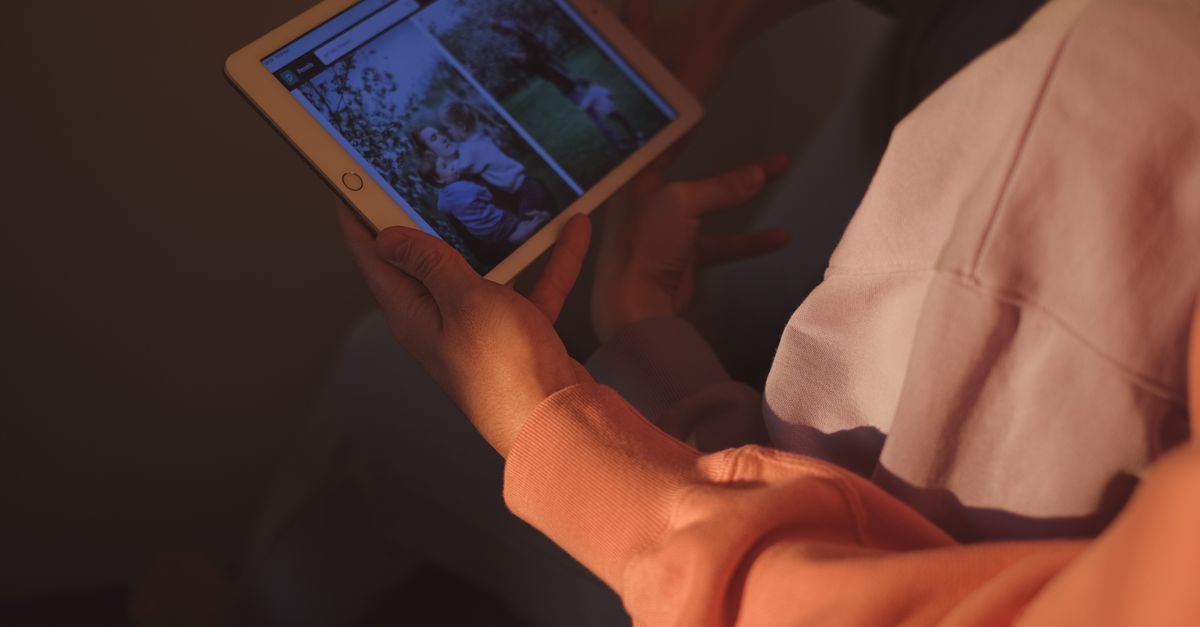 Hands holding a tablet device indoors, browsing photos with warm lighting.