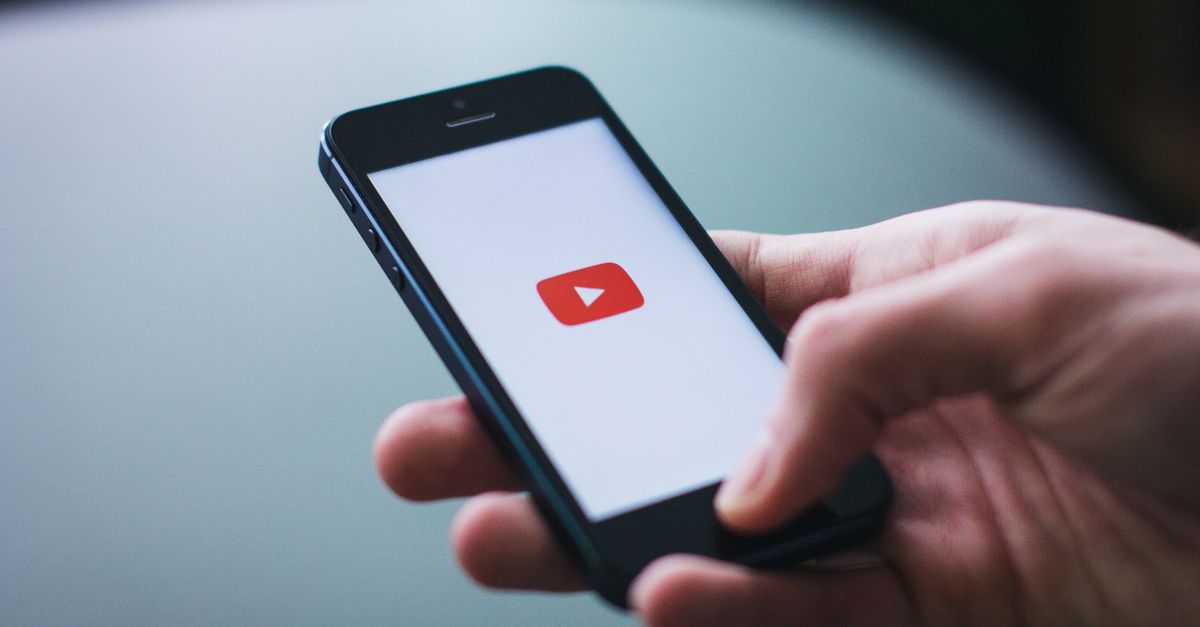 Close-up of a hand holding a smartphone displaying the YouTube app on the screen.