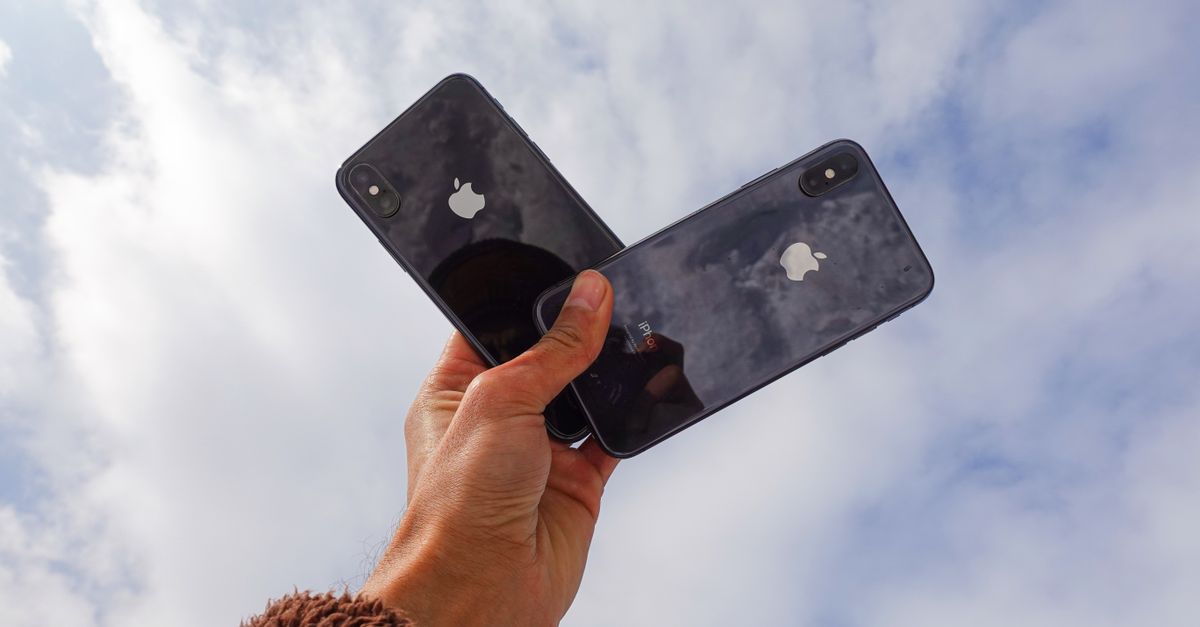 Close-up of a hand holding two smartphones against a cloudy sky, showcasing modern technology.