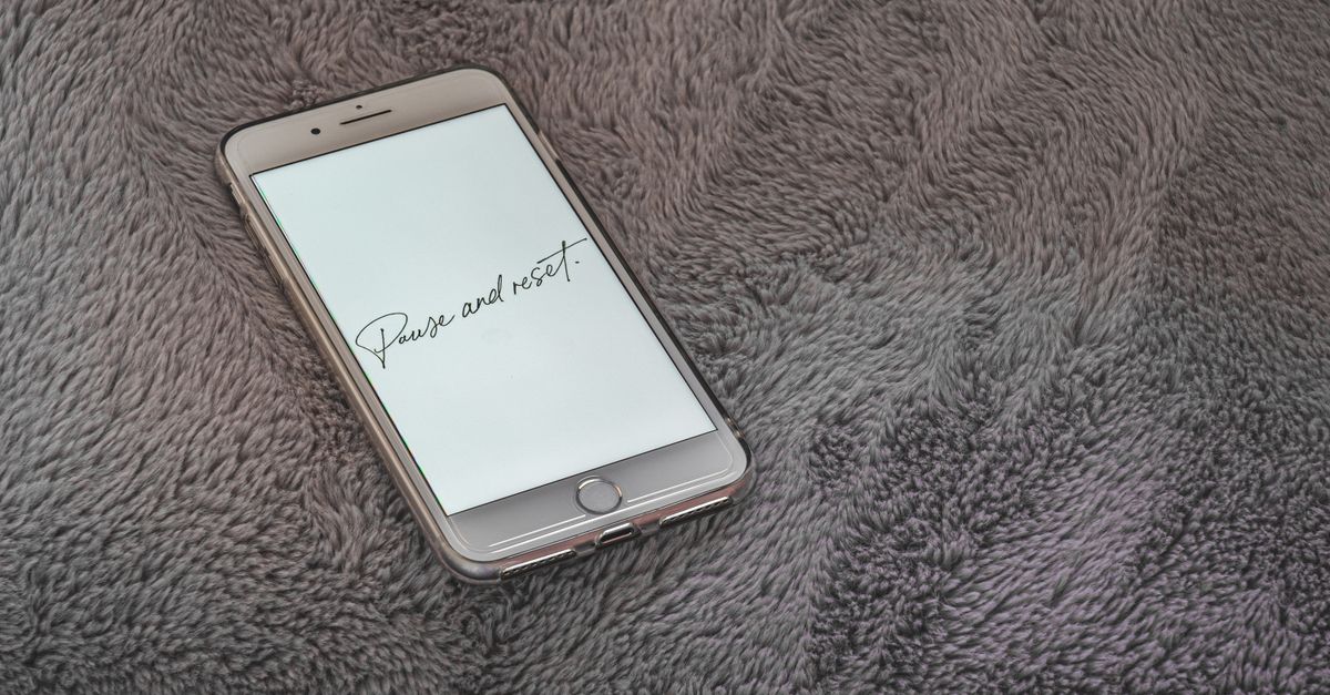 A smartphone displaying 'Pause and reset' message on a soft grey textured surface.