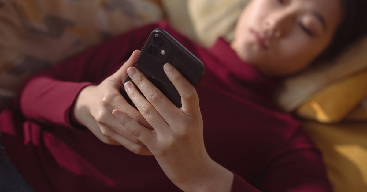 スマートフォンを手に横になる女性、隠しフォルダアプリの写真トラブルを扱う記事