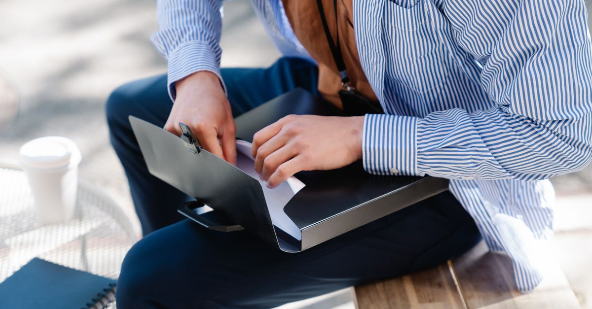 Professional reviewing documents in a folder while sitting outside, dressed in business attire.