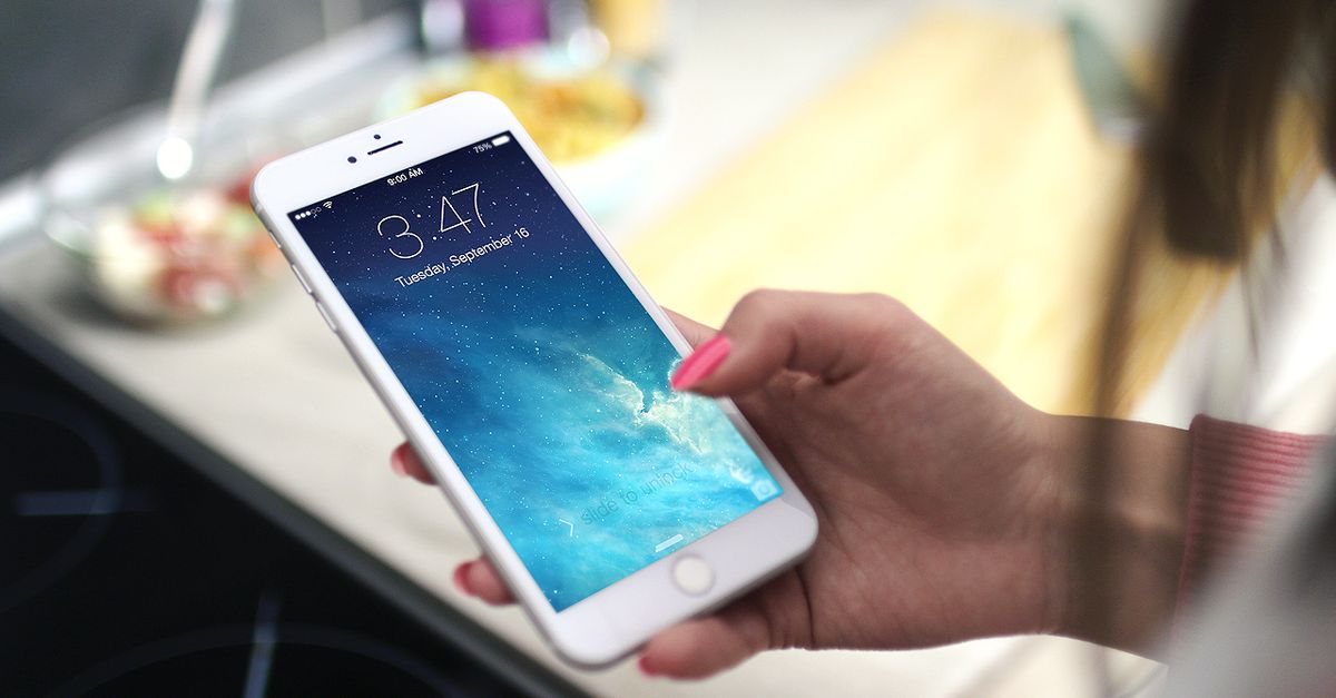 Close-up shot of a person holding a smartphone in a kitchen setting, displaying the lock screen.