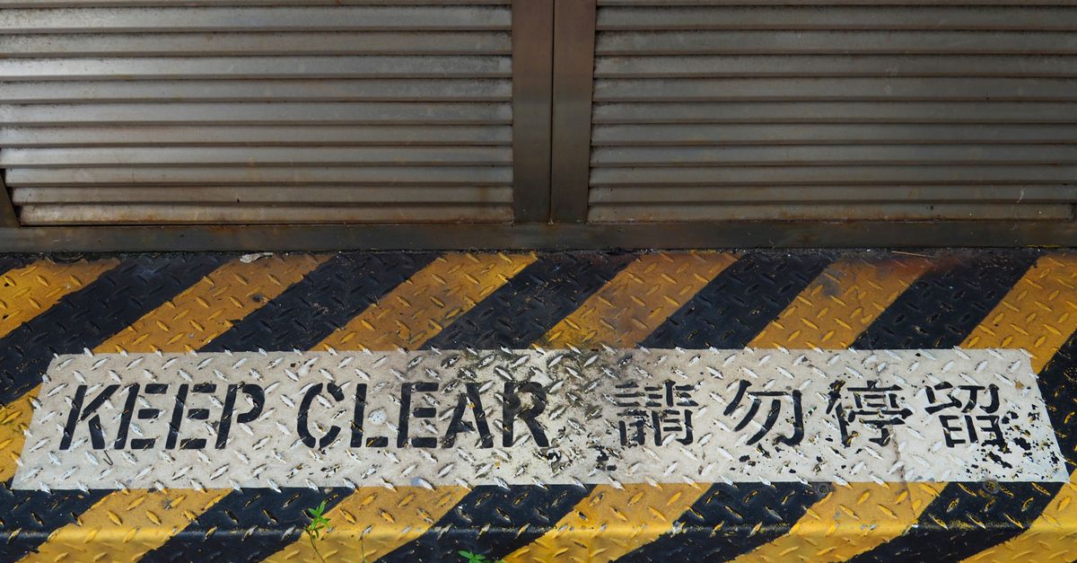 A bilingual 'Keep Clear' safety sign on a rusty metal floor in Hong Kong.
