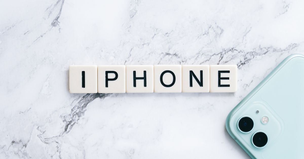 Flatlay of scrabble tiles spelling iPhone next to a smartphone on a marble surface.