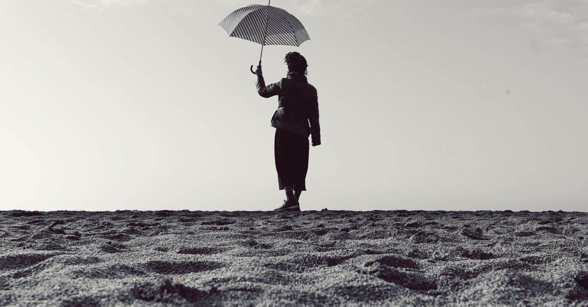 Black and white silhouette of a woman holding an umbrella while standing on a serene beach.