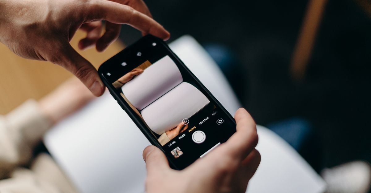 Person using smartphone to photograph blank open book. Concept of mobile photography and creativity.
