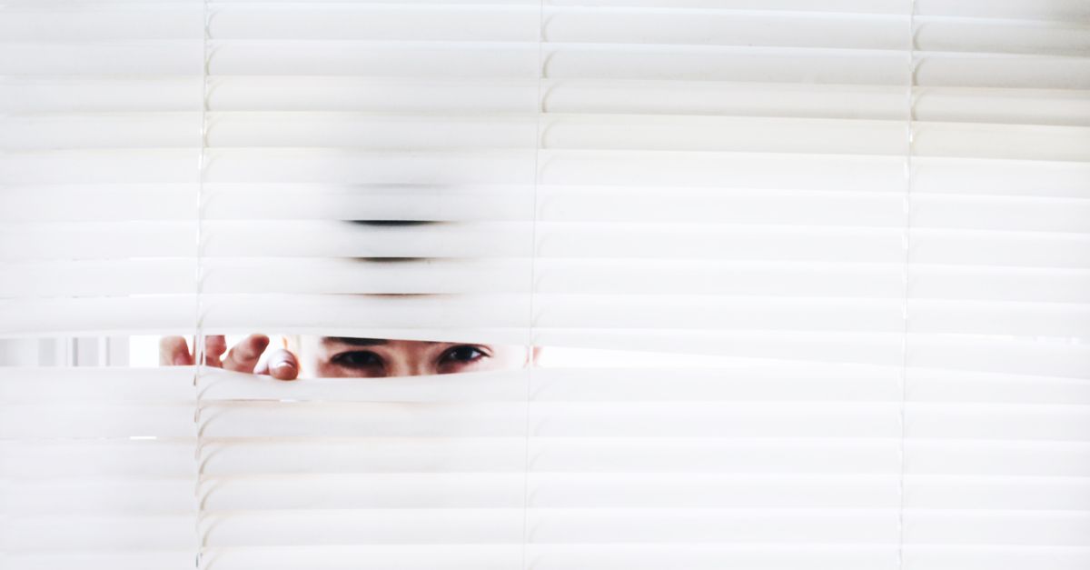 A person peeks through white blinds, creating an intriguing sense of curiosity.