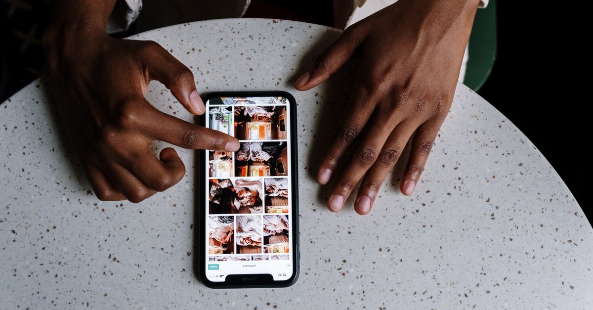 Hands interacting with smartphone displaying social media content on table in cafe setting.
