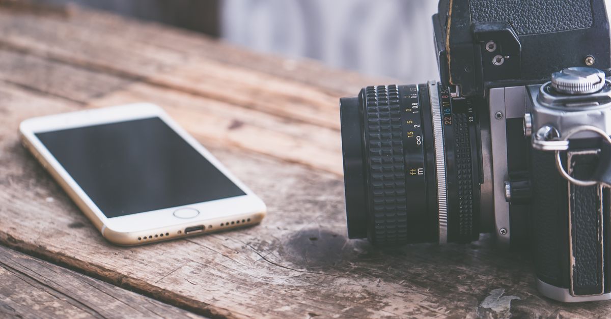 A vintage camera alongside a smartphone on a rustic wooden table surface.