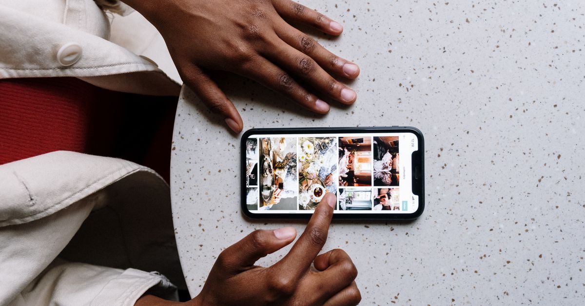 Close-up of hands using a smartphone on a cafe table, browsing social media or photos.