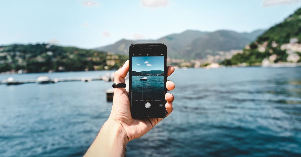 A person photographing a beautiful lake view using a smartphone, showcasing modern technology in nature.