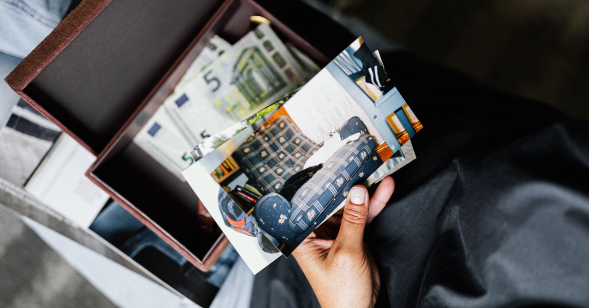 A hand holds nostalgic photos over a box filled with more images and keepsakes.