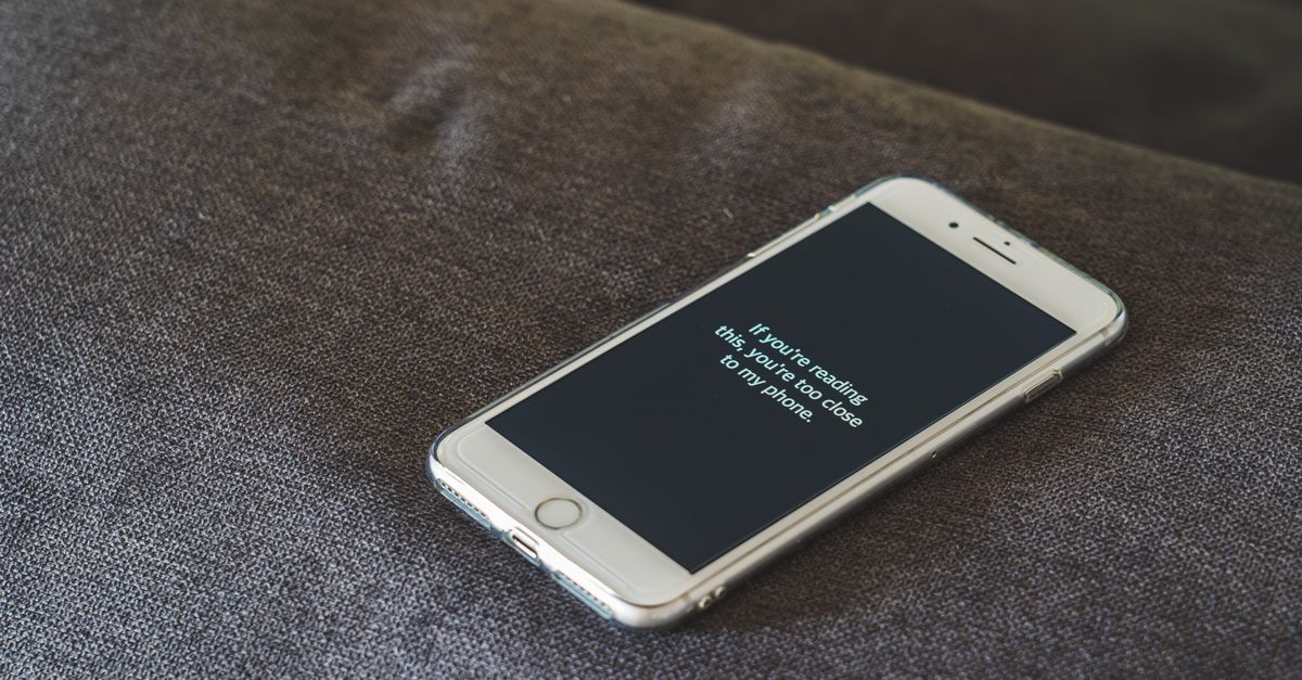 A smartphone with a humorous lock screen message placed on a grey couch, emphasizing privacy.