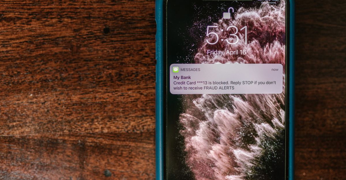 Close-up of smartphone displaying a fraud alert message on wooden surface.