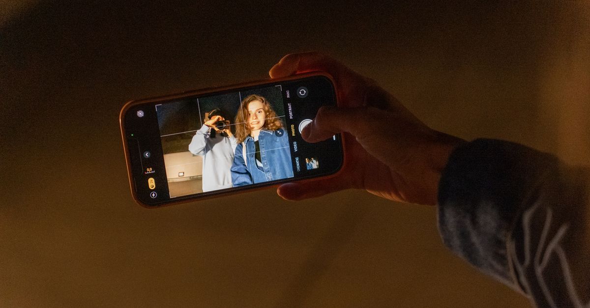 A couple capturing a romantic memory using a smartphone camera during nighttime indoors.