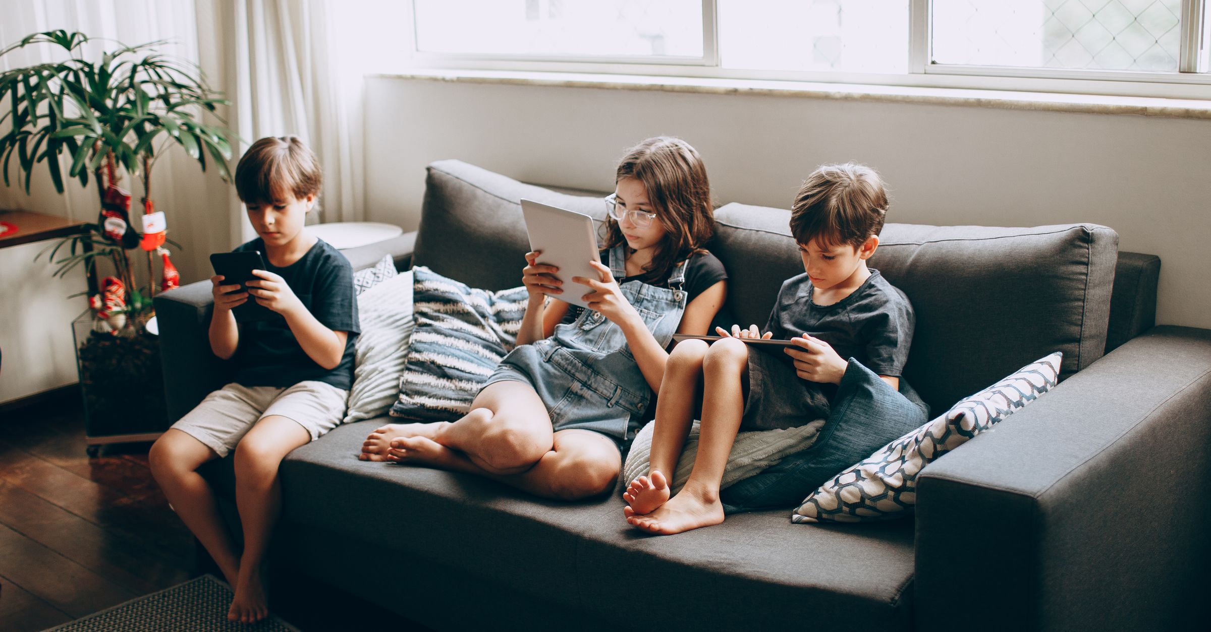 Three children using devices on a sofa, illustrating shared-device privacy for an iPhone photo vault.