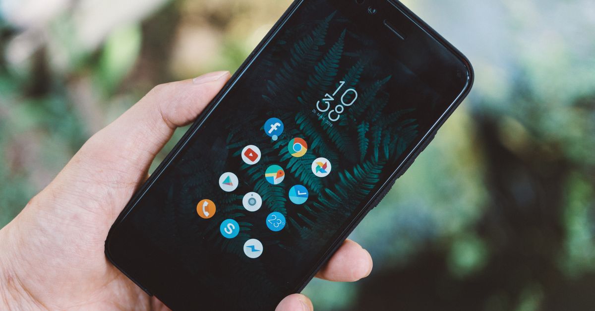 Close-up of a hand holding a smartphone with app icons and a nature wallpaper.