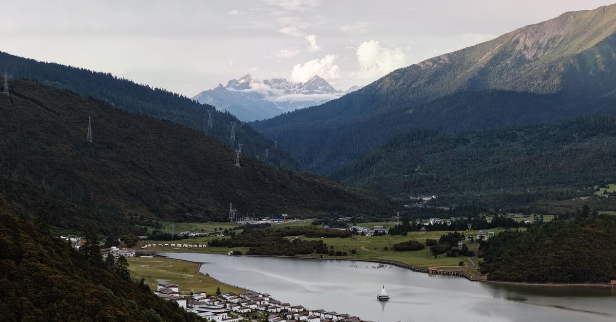 Beautiful valley in Tibet with a river, traditional houses, and snow-capped mountains in the distance.