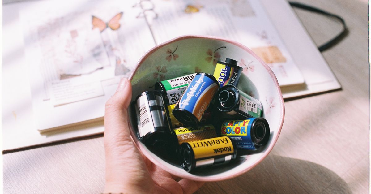 A hand holding a bowl filled with various vintage film rolls on a sunlit table.