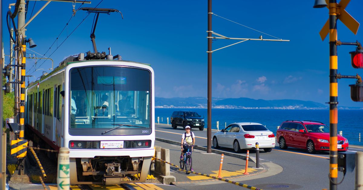 A vibrant scene of a tram crossing by the coast in Kamakura, Japan, with cyclists and cars nearby.