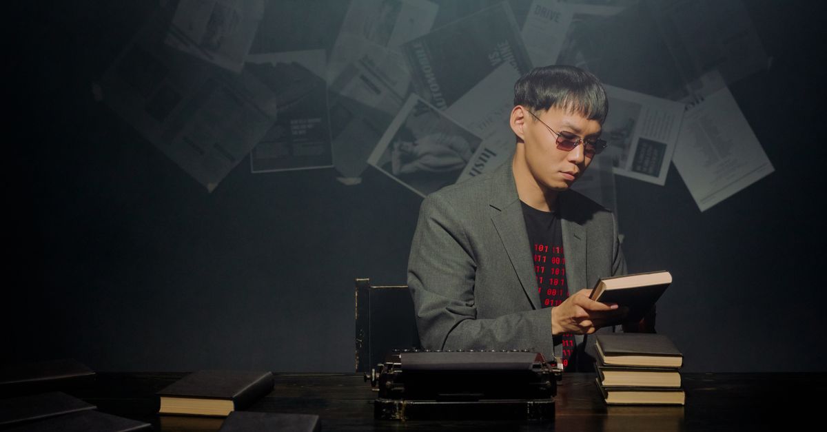 A serious man engrossed in a book, surrounded by stacks of notebooks and a typewriter.